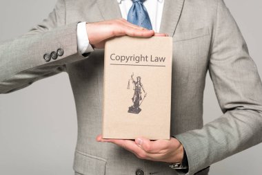 cropped view of lawyer holding book with copyright law title isolated on grey clipart