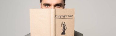 serious lawyer obscuring face with copyright law book isolated on grey clipart