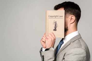 Gri üzerine izole edilmiş telif hakkı kitabıyla yüzünü gizleyen avukatın kenar görüşü