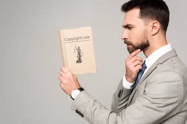 side view of serious lawyer reading book with copyright law title isolated on grey clipart