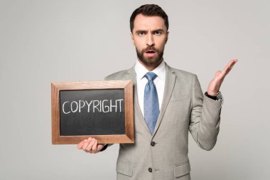 Gri üzerinde telif hakkı yazıtları olan kara tahtayı tutarken kameraya bakan hoşnutsuz işadamı