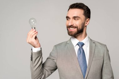 smiling businessman holding light bulb isolated on grey clipart