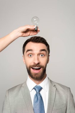 Heyecanlı iş adamının kafasının üstünde ampulü tutan kadının gri renkte izole edilmiş görüntüsü.