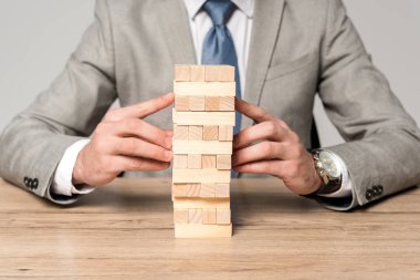 Gri üzerine izole edilmiş tahta kule oyunu oynayan işadamının kırpılmış görüntüsü