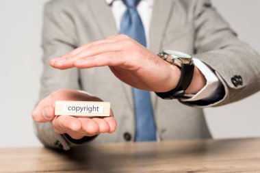 cropped view of businessman covering wooden block with word copyright with hand isolated on grey clipart