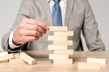 Gri üzerine izole edilmiş tahta kule oyunu oynayan işadamının kırpılmış görüntüsü