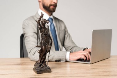 partial view of lawyer using laptop near themis statue isolated on grey clipart