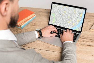 cropped view of businessman using laptop with map on screen isolated on grey clipart