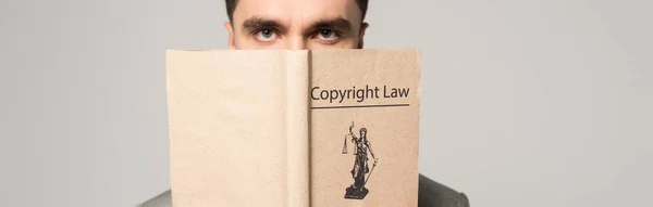 serious lawyer obscuring face with copyright law book isolated on grey