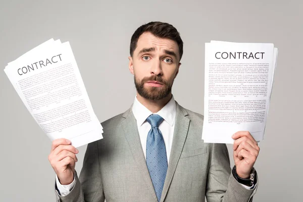 Mutsuz iş adamı sözleşmeleri tutuyor ve gri kameraya bakıyor.