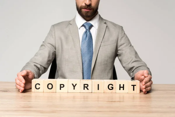 木製の立方体の近くの机に座っているビジネスマンのクロップドビューグレーに隔離された言葉の著作権 — ストック写真