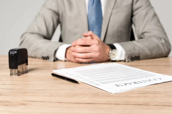 灰色に隔離された契約書切手ペンの近くのデスクに座っているビジネスマンのクロップドビュー — ストック写真