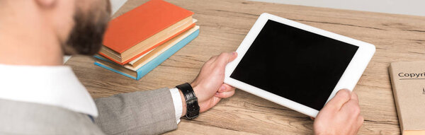 partial view of businessman holding digital tablet with blank screen isolated in grey, panoramic shot