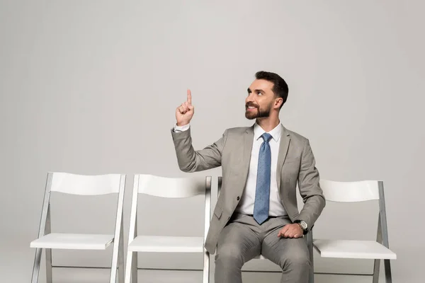 Hombre Negocios Sonriente Sentado Silla Mostrando Gesto Idea Aislado Gris — Foto de Stock