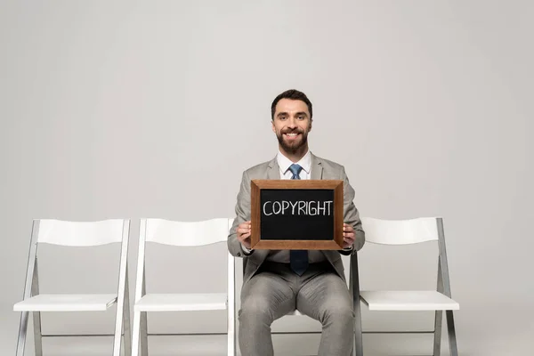 Sorridente Empresário Segurando Quadro Com Palavra Copyright Enquanto Sentado Cadeira — Fotografia de Stock