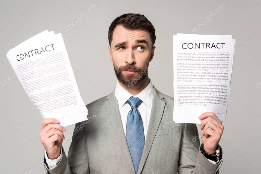 skeptical businessman holding contracts and looking away isolated on grey