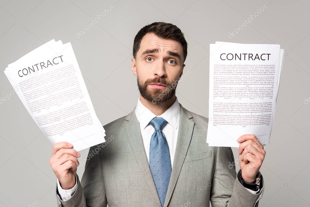 upset businessman holding contracts and looking at camera isolated on grey