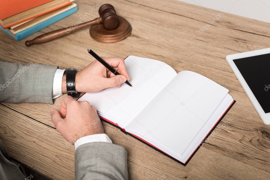 cropped view of lawyer writing in notebook on wooden desk