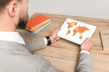 Gri ekranda dünya haritası olan dijital tablet kullanan işadamının kırpılmış görüntüsü