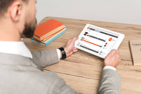 КИЕВ, Украина - 25 ноября 2019 года: обрезанный вид бизнесмена с помощью цифрового планшета с приложением Soundcloud на экране изолирован на сером
