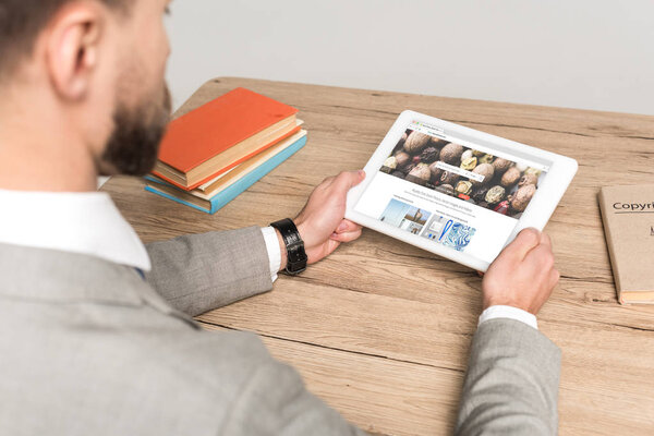 КИЕВ, Украина - 25 ноября 2019 года: обрезанный вид бизнесмена с помощью цифрового планшета с приложением Depositphotos на экране изолирован на сером
