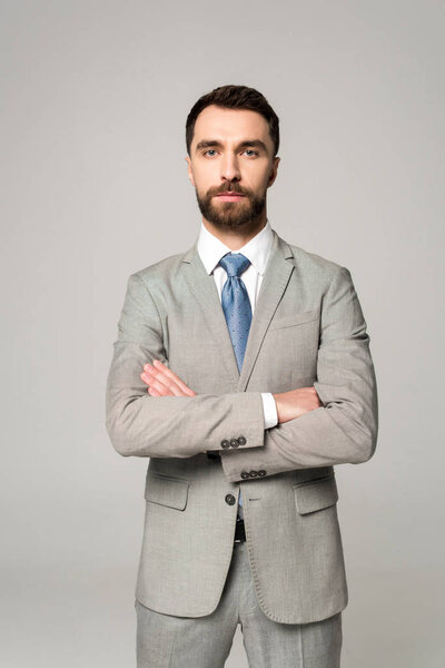 serious businessman standing with crossed arms and looking at camera isolated on grey