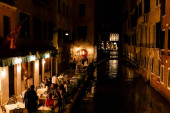 Benátky, Itálie - 24. září 2019: turisté sedí v blízkosti venkovní kavárny s výhledem na průplav v noci v Benátkách, Itálie 