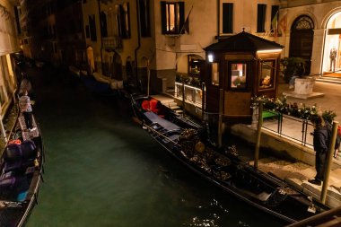 VENICE, ITALY - SEPTEMBER 24, 2019: canal with gondolas near ancient building at night in Venice, Italy  clipart