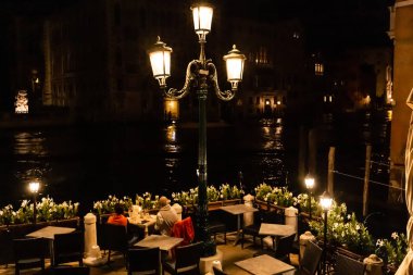 Venedik, İtalya - 24 Eylül 2019: Venedik, İtalya 'da geceleri masada oturup kanallara bakan turistler 