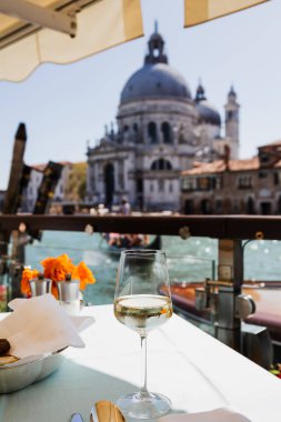 selective focus of wine glass on table and Santa Maria della Salute church on background  clipart