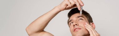 sexy man using eye drops isolated on grey, panoramic shot clipart