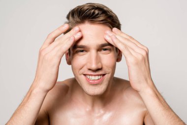 Güler yüzlü seksi adam kaslı gövdesi ve mükemmel cildi ile Gri üzerinde izole edilmiş yüze dokunuyor.