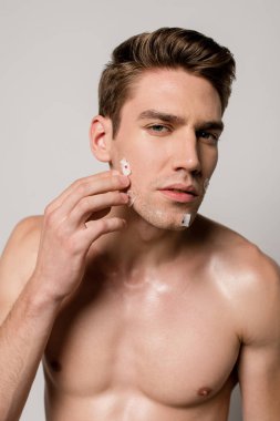 sexy man with muscular torso touching bloody wounds after shaving on face isolated on grey clipart