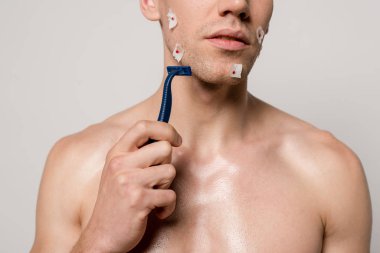 Traş makinesini gri renkte tuttuktan sonra kaslı gövdesi ve kanlı yaraları olan seksi adamın kırpılmış görüntüsü.