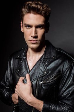 sexy young man in biker jacket  looking at camera on black background clipart