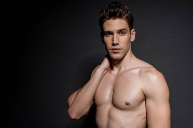 Siyah arka planda poz veren kaslı vücutlu genç ve seksi bir adam.