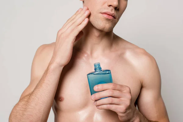 グレーに単離された剃り化粧水の後に適用される筋肉の胴を持つセクシーな男のクロップドビュー — ストック写真