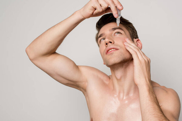 sexy man with bare torso using eye drops isolated on grey