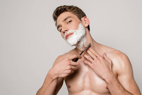 sexy man with muscular torso shaving with straight razor isolated on grey