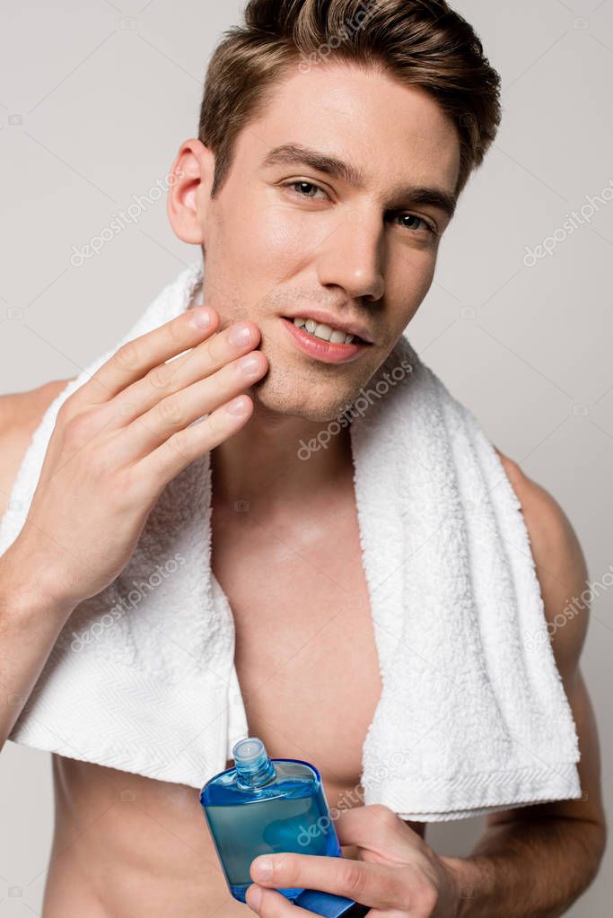 sexy man with muscular torso with after shave lotion and towel touching face isolated on grey