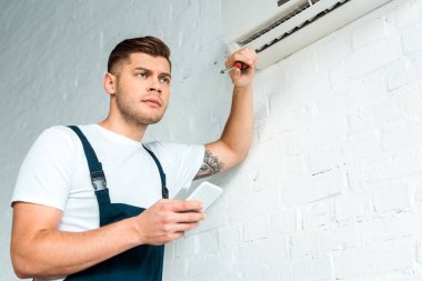 Klimanın yanında akıllı telefon kullanan dalgın bir kurucu 