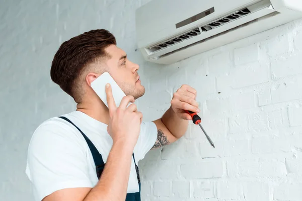 Gutaussehender Installateur Schaut Auf Klimaanlage Während Mit Smartphone Spricht Und — Stockfoto