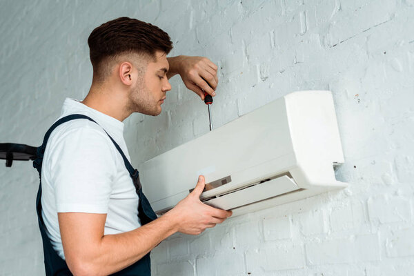 handsome installer holding screwdriver while installing air conditioner 
