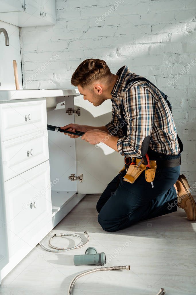 side view of installer standing on knees while working near kitchen cabinet 