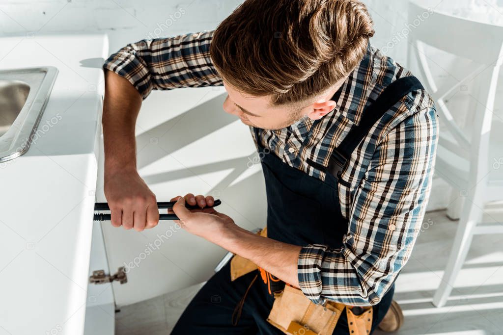 installer holding slip joint pliers while working near kitchen cabinet 