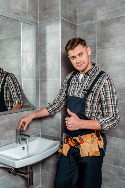 installer standing near faucet with flowing water and showing thumb up clipart