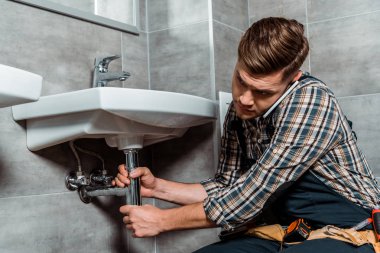 installer touching pipe while talking on smartphone in bathroom  clipart