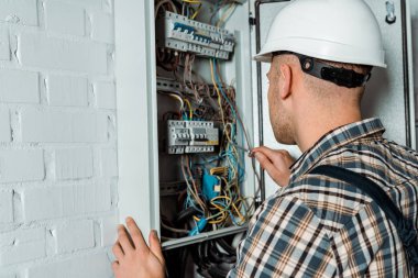 Güvenlik kasklı elektrikçi elinde tornavidayla santralin yanında.  