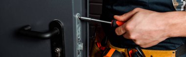 panoramic shot of installer holding screwdriver near door handle  clipart