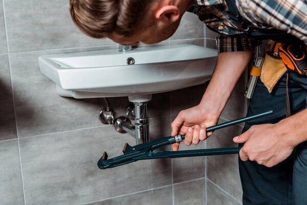 selective focus of installer holding slip joint pliers near pipe in bathroom 